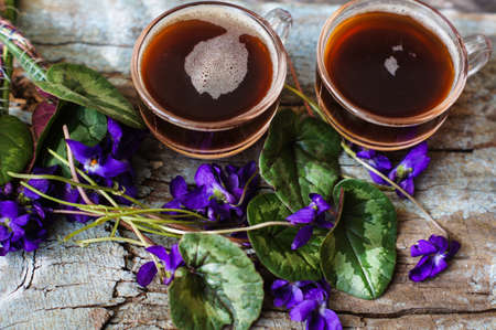 First spring flowers of violets and cup of coffee on the old wooden table