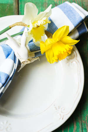 Spring festive easter dining table setting with yellow daffodil flowers,  napkins and vintage cutlery on a wooden boardの写真素材