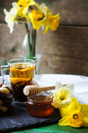 Cup of tea with cookies on the bright napkin, a mug with honey and daffodil flowersの写真素材