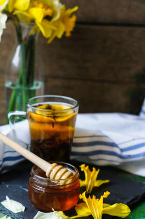 Cup of tea with cookies on the bright napkin, a mug with honey and daffodil flowersの写真素材