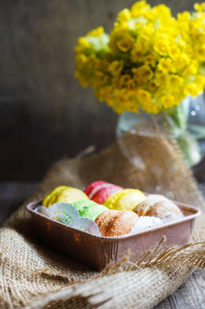 Colorful macaroons and first spring flowers on old wooden background