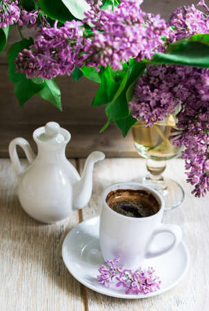 Lilac flowers in a vase and cup of coffee on the rustic style backgroundの写真素材