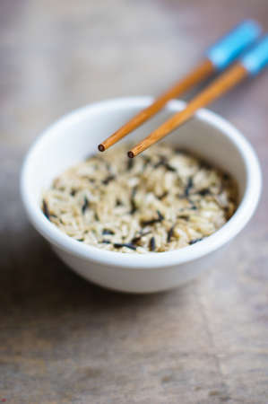 bowl of rice with wooden chopsticks and a wood place mat