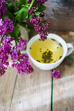 Lilac flowers in a pot and cup of tea in rustic interiorの写真素材