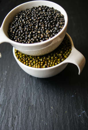 Different types of beans in the white bowls on the black stone backgroundの写真素材