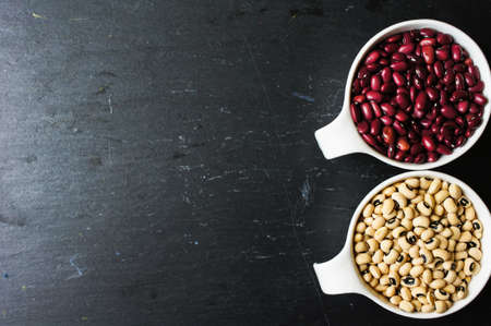 Different types of beans in the white bowls on the black stone backgroundの写真素材