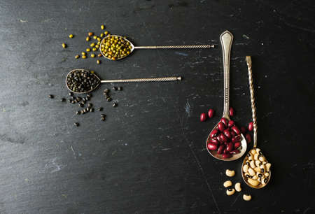 Different types of beans in the vintage spoons on the black stone backgroundの写真素材