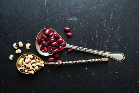 Different types of beans in the vintage spoons on the black stone backgroundの写真素材