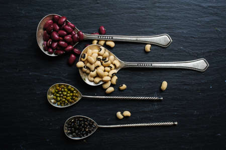 Different types of beans in the vintage spoons on the black stone backgroundの写真素材