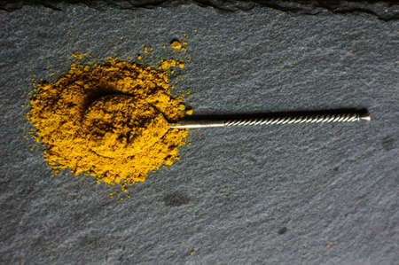 ground turmeric or curcuma in silver vintage spoon on black stone surfaceの写真素材
