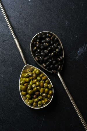 Different types of beans in the vintage spoons on the black stone backgroundの写真素材