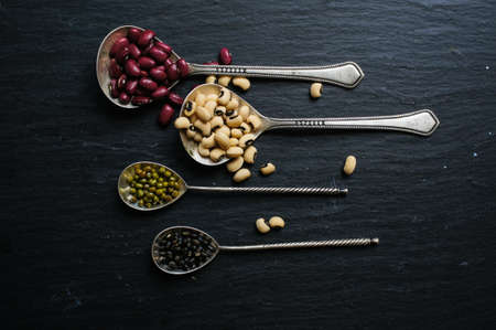 Different types of beans in the vintage spoons on the black stone backgroundの写真素材