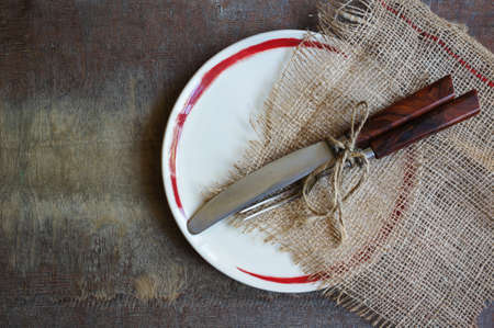 Plate and silverware on the old wooden table with burlap and napkinの写真素材