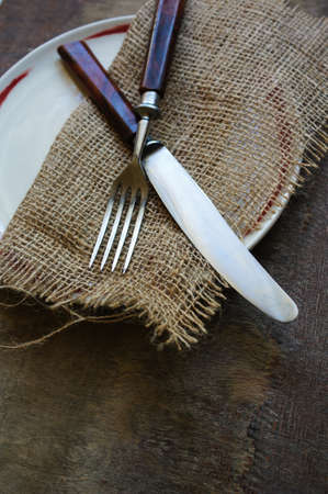 Plate and silverware on the old wooden table with burlap and napkinの写真素材