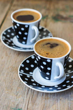 Black and white dots cup of coffee on the old wooden table with coffee beans, cinnamon sticks and anise starの写真素材