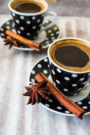 Black and white dots cup of coffee on the old wooden table with coffee beans, cinnamon sticks and anise starの写真素材