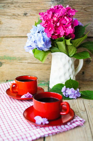 Hydrangea flowers in a vase and cup of coffee on the wooden tableの写真素材
