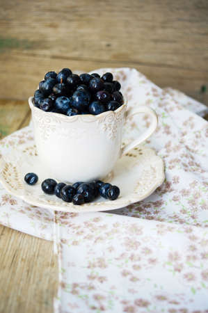 Fresh blueberries in vintage bowl and bright napkin on old wooden tableの写真素材