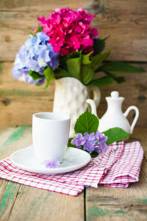 Hydrangea flowers in a vase and cup of coffee on the wooden tableの写真素材