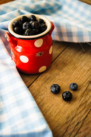 Fresh blueberries in vintage bowl and bright napkin on old wooden tableの写真素材