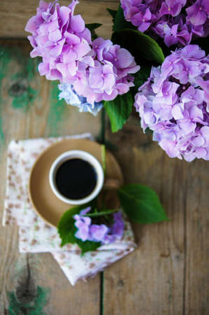 Hydrangea flowers in a vase and cup of coffee on the wooden tableの写真素材