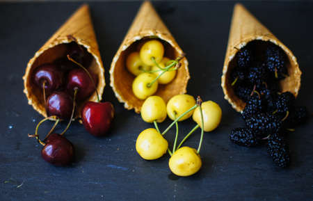 Fresh fruits in the ice cream cone on wooden background,selective focusの写真素材