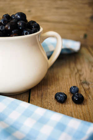 Fresh blueberries in vintage bowl and bright napkin on old wooden tableの写真素材
