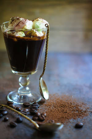 Cup of black coffee and marshmallows with chocolate over them, and coffee beans on the stone dark...