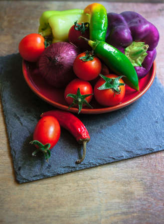 Ripe fresh vegetable cherry tomatoes, bell and chilli peppers, onion, rustic backgroundの写真素材