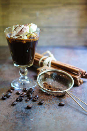 Cup of black coffee and marshmallows with chocolate over them, and coffee beans on the stone dark...