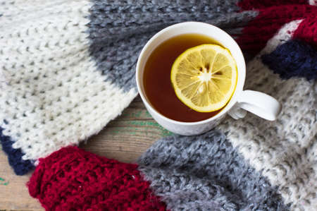 Winter time: cup of hot tea with lemon and scarf on rustic backgroundの写真素材