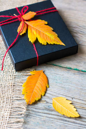 Present box decorated with autumnal yellow leaveas and berries on rustic backgroundの写真素材
