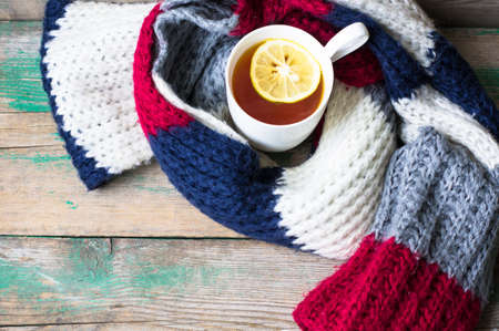 Winter time: cup of hot tea with lemon and scarf on rustic backgroundの写真素材
