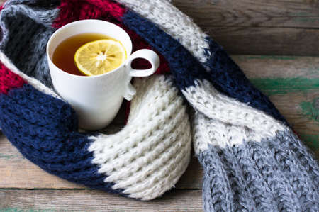 Winter time: cup of hot tea with lemon and scarf on rustic backgroundの写真素材