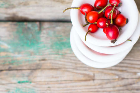 Ripe rose hips in the ceramic bowl on a rustic backgroundの写真素材
