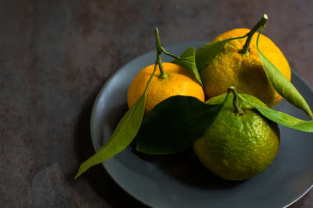 Ripe tangerines with green leaves on dark rustic backgroundの写真素材