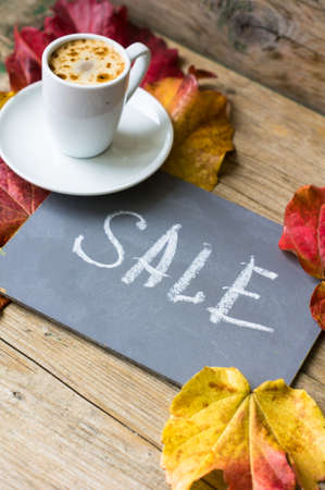 Note with Sale word on the chalkboard, cup of coffee and bright colors ivy plant leaves on wooden...