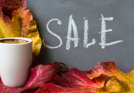Note with Sale word on the chalkboard, cup of coffee and bright colors ivy plant leaves on wooden backgroundの写真素材