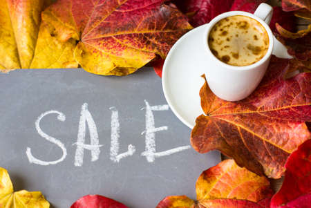 Note with Sale word on the chalkboard, cup of coffee and bright colors ivy plant leaves on wooden backgroundの写真素材