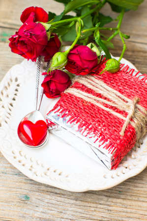 Table setting for St. Valentines day with glasses of wine, present box and red roses  in rustic styleの写真素材