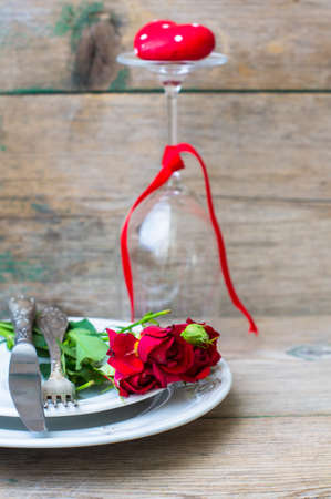 Table setting for St. Valentines day with glasses of wine, present box and red roses  in rustic styleの写真素材