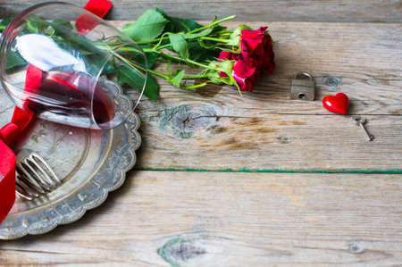Table setting for St. Valentines day with glasses of red wine, present box and red roses  in rustic styleの写真素材