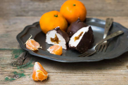 Ripe tangerines and marshmallow covered with chocolate on vintage plate on rustic wooden tableの写真素材