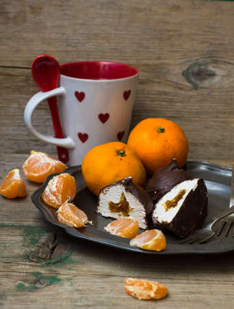 Ripe tangerines and marshmallow covered with chocolate on vintage plate on rustic wooden tableの写真素材