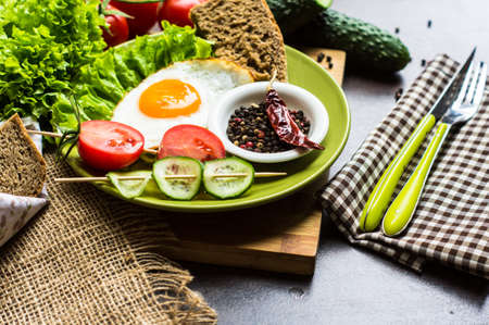 Breakfast with fried egg, cherry-tomatoes and spices on rustic kitchen tableの写真素材