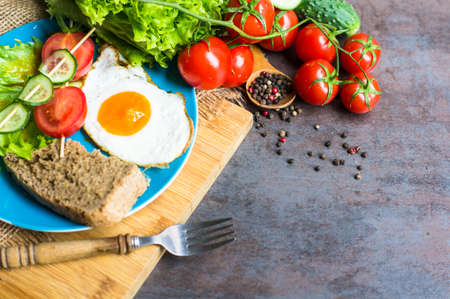 Breakfast with fried egg, cherry-tomatoes and spices on rustic kitchen tableの写真素材