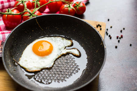 Breakfast with fried egg, cherry-tomatoes and spices on rustic kitchen table