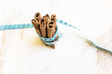 Weight loss concept with  cinnamon sticks and measure tape on rustic wooden backgrounfの写真素材