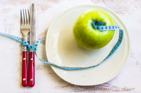 Weight loss concept with vintage plate, silverware and green apple on rustic wooden backgrounf