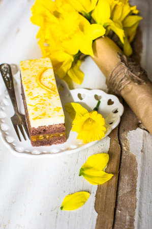 Orange cake and bright yellow daffodil flowers on rustic background